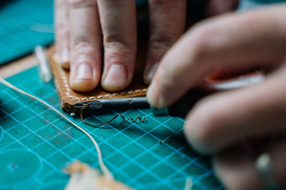 Detailed view of hands stitching leather on cutting board, reflecting craftsmanship in a workshop.